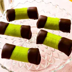 Fem gröna dammsugare bakverk med chokladtoppar ligger på ett glasfat.