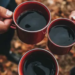Händer håller röda muggar med varmt kaffe. En mysig stund utomhus, perfekt för att koka kaffe.