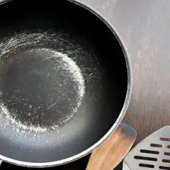 En sliten teflonpanna med repor och en träspatel samt en metallspatel ligger på en mörk träyta. Dags att diska!