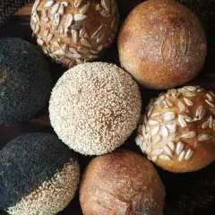 En samling nybakade surdegsbröd med vete, toppade med vallmofrön, sesamfrön och solrosfrön.