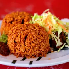 Två portioner jollof rice med sallad och en kryddig sås. En smakrik rätt som lockar.