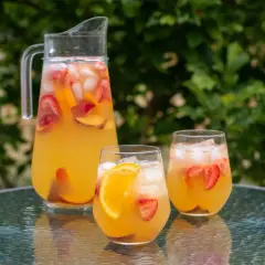 En karaff och två glas med uppfriskande cava sangria fylld med frukt och is, redo att avnjutas utomhus.