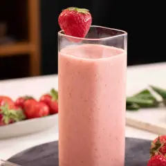 En härlig jordgubbssmoothie utan banan, dekorerad med en färsk jordgubbe. Bredvid står en skål med fler jordgubbar.