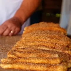 En hand lägger socker och kanel på en stapel nygjorda churros. Dessa friterade godsaker är ett populärt sätt att svara på frågan "vad är churros".