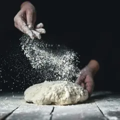 Händer strör mjöl över deg. Vete och råg ger en härlig doft av nybakat bröd.