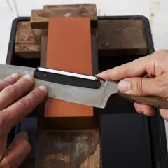 Händer slipar kniv på en röd sten. En vass egg är viktig för matlagning.