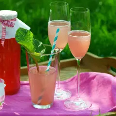 En flaska rabarberdrink och två glas prosecco på en bricka i gräset. En härlig sommardrink!