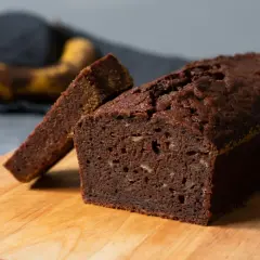 En saftig banan sockerkaka med en skiva uppskuren, redo att avnjutas. En övermogen banan ligger i bakgrunden.