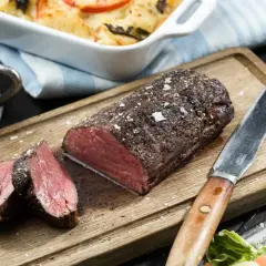 En saftig, helstekt oxfile med perfekt rosa kärna, serverad på en träskärbräda med en skål fylld med mörk sås och en fräsch sallad.