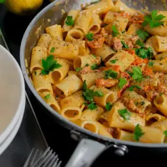 En krämig salsiccia pasta med rigatoni, toppad med färsk persilja och nymalen svartpeppar. En portion serveras i en vit skål.