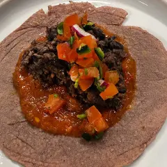 En lila tortilla med en klick refried beans, salsa och hackade grönsaker.