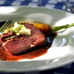 Skivat flat iron steak med en klick vitlöksdressing och en grön sparris.