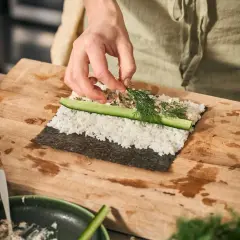 Händer lägger dill på ris och gurka för ett sushi recept.