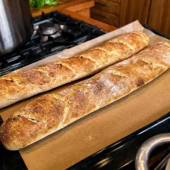 Två gyllenbruna surdegsbaguetter på bakplåtspapper, redo att avnjutas. Ett perfekt surdegsbaguette recept!