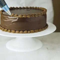En chokladtårta dekoreras med en sprits med chokladfrosting. Ett perfekt resultat med detta ganache recept.