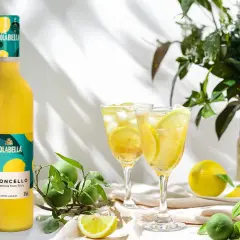 En flaska Isolabella Limoncello står bredvid två glas med is och citron. Perfekt för ett somrigt limoncello recept.