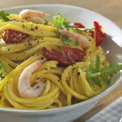 En skål med gyllene zafferano pasta med räkor, soltorkade tomater och ruccola. En härlig måltid!