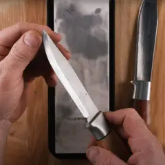 Händer som håller en kniv över en slipsten, visar hur slipar man knivar för att få en vass egg. En annan kniv ligger bredvid.