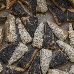 En hög med nybakade surdegsbröd, vissa toppade med sesamfrön, andra med vallmofrön.