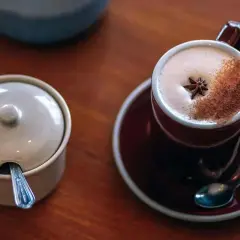 En kopp värmande chai latte med stjärnanis och kanel, perfekt för ett mysigt chai latte recept. Bredvid står en sockerskål med sked.