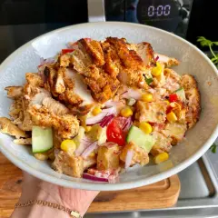 En skål med kyckling kebab, potatissallad, majs, gurka, tomat och rödlök. En läcker och mättande måltid.