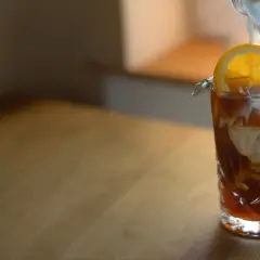En hand häller mjölk i ett glas med iskaffe, garnerat med en apelsinskiva. Ett perfekt iskaffe recept för en varm dag.