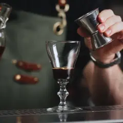 En bartender häller upp en mörk vätska i ett glas, kanske för att skapa en Leonard Sachs drink.