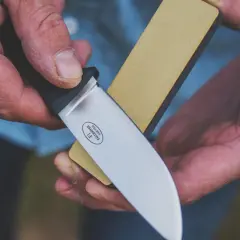 Händer som bryna kniv med en slipsten.