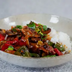 En skål med ris och en smakrik kyckling cashew-röra med paprika och svamp, toppad med salladslök.