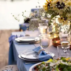 Vacker dukning vid vattnet för ett somrigt mat midsommar. Blommor, ljus och tallrikar redo för fest.