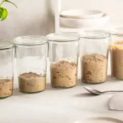 Fem glasburkar visar hur surdeg av råg utvecklas, från en kompakt massa till en bubblig och aktiv kultur.