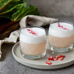 Två glas med en krämig rabarber sour, toppad med skum och strödd med rabarberpulver. En härlig sommardrink!