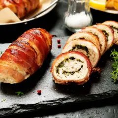 En hel och skivad baconlindad kyckling med örter, serverad på en svart stenplatta med timjan.