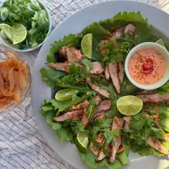 Grilla pluma serveras i salladsblad med lime, koriander och en krämig dipp. Kimchi och salladslök i skålar bredvid.