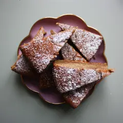 Skivor av saftig banankaka, pudrade med florsocker, ligger på en lila tallrik. Perfekt för fikat, detta är nog den godaste banankakan!