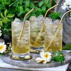 Tre glas med is och gyllene sugrör. En uppfriskande geting drink i en lummig trädgård.