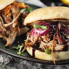 Två saftiga pulled pork burgare med rödlök och groddar på en mörk tallrik.