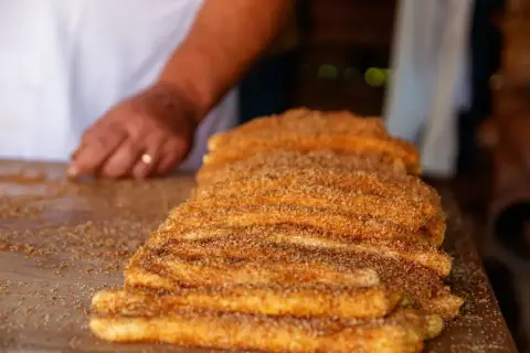 En hand lägger socker och kanel på en stapel nygjorda churros. Dessa friterade godsaker är ett populärt sätt att svara på frågan "vad är churros".