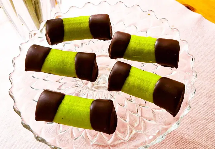 Fem gröna dammsugare bakverk med chokladtoppar ligger på ett glasfat.