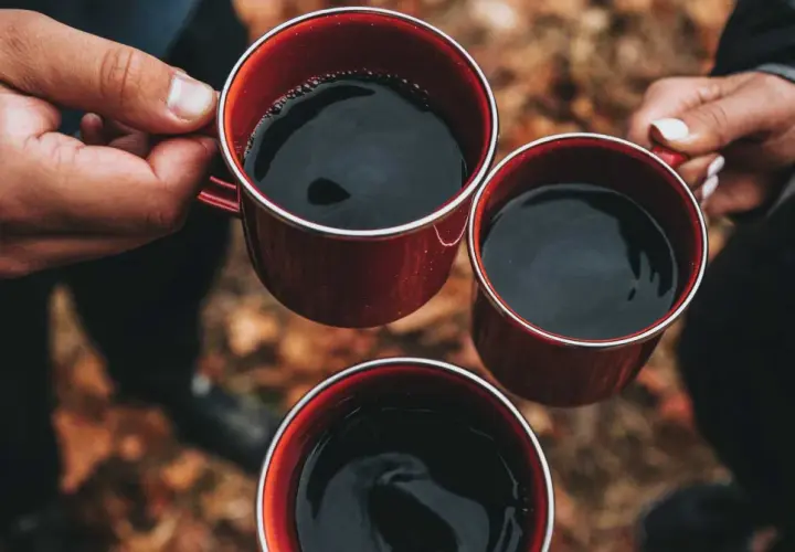 Händer håller röda muggar med varmt kaffe. En mysig stund utomhus, perfekt för att koka kaffe.