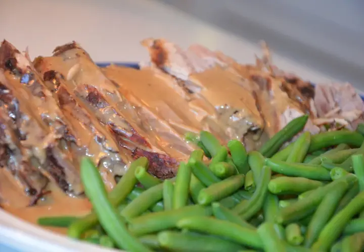 Skinkstek i gryta, saftig och uppskuren, serveras med en krämig sås och gröna bönor. En klassisk och smakrik rätt.