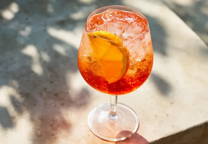 Ett glas med en bubblig Aperol Spritz, fylld med is och en apelsinskiva. Perfekt för en solig dag.