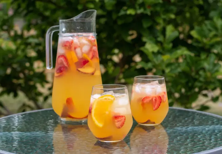 En karaff och två glas med uppfriskande cava sangria fylld med frukt och is, redo att avnjutas utomhus.