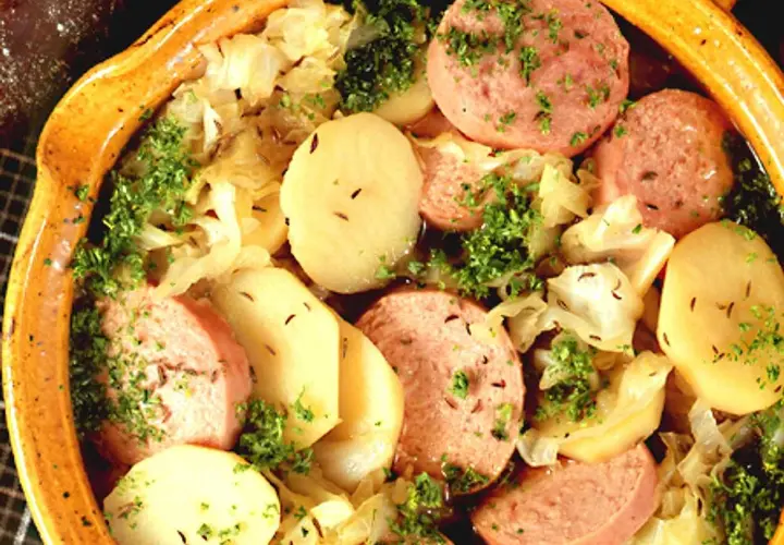 En värmande korvgryta med potatis, kål och persilja i en rustik keramikskål.