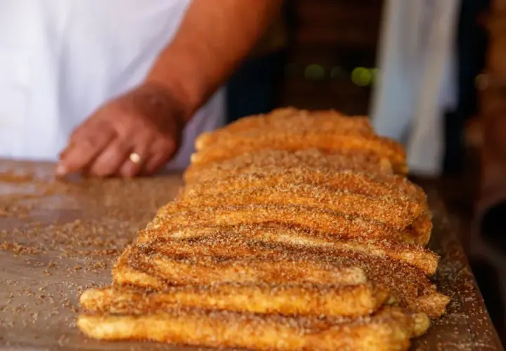 En hand lägger socker och kanel på en stapel nygjorda churros. Dessa friterade godsaker är ett populärt sätt att svara på frågan "vad är churros".
