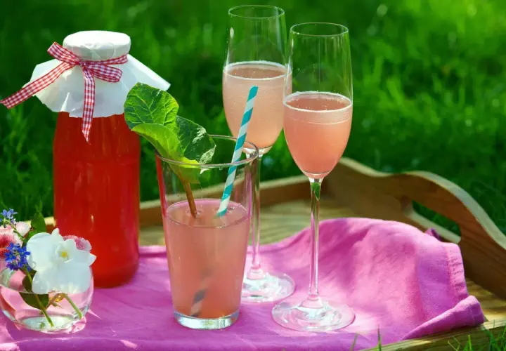 En flaska rabarberdrink och två glas prosecco på en bricka i gräset. En härlig sommardrink!