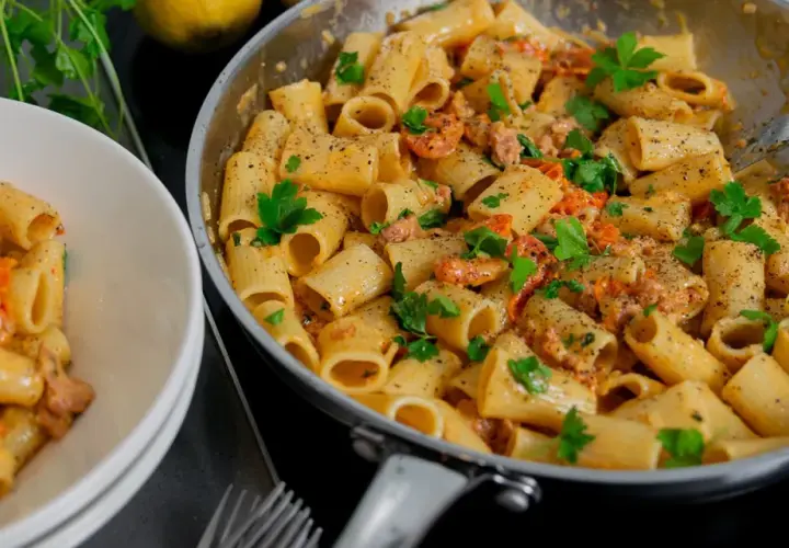 En krämig salsiccia pasta med rigatoni, toppad med färsk persilja och nymalen svartpeppar. En portion serveras i en vit skål.