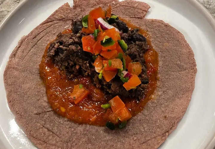 En lila tortilla med en klick refried beans, salsa och hackade grönsaker.