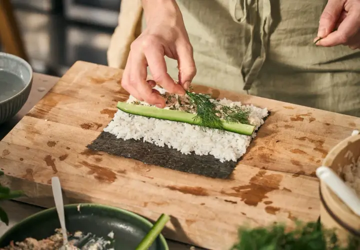 Händer lägger dill på ris och gurka för ett sushi recept.