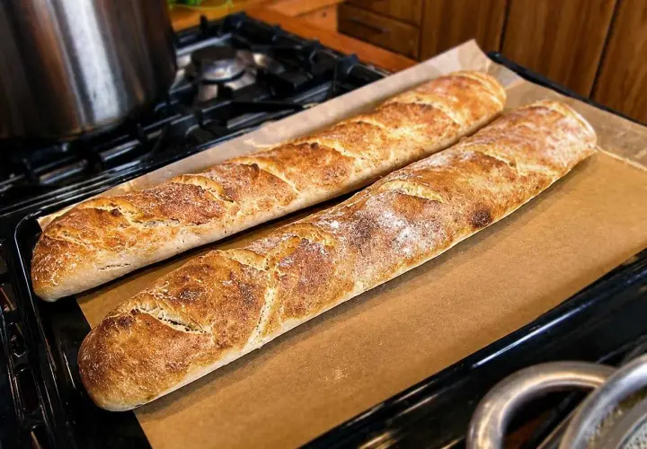 Två gyllenbruna surdegsbaguetter på bakplåtspapper, redo att avnjutas. Ett perfekt surdegsbaguette recept!